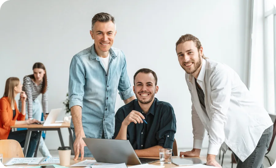 Three colleagues smiling over a laptop in a bright open-plan office